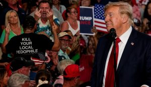 BREAKING: Trump gets a BRUTAL message at his own rally as heckler gives him a double middle finger –  right behind a man wearing a “KILL YOUR LOCAL PEDOPHILE” T-shirt!
